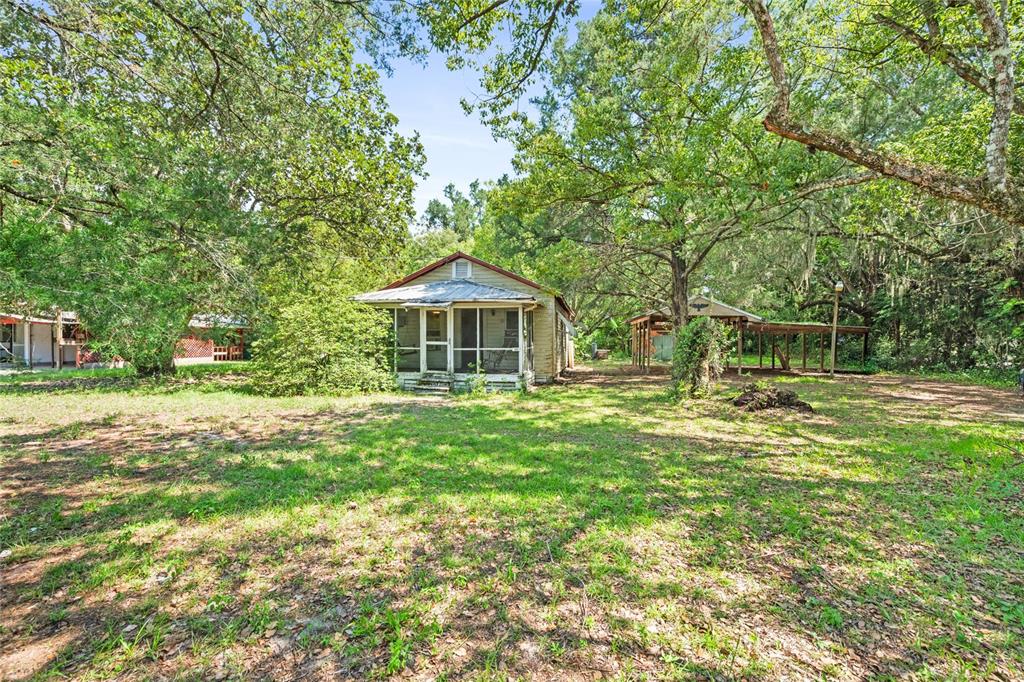 A small, weathered house with a screened-in porch sits on a grassy, tree-shaded lot — 140 W PONKAN ROAD, APOPKA, FL