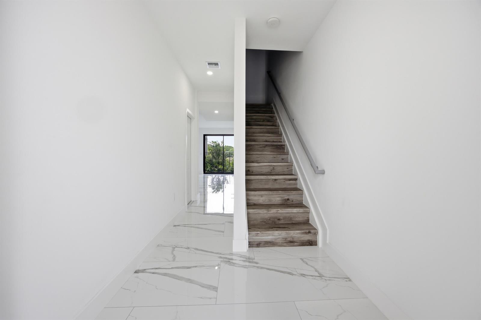 A bright hallway features white marble-look tile flooring and a wooden staircase with a handrail — 1544 NW 1st Avenue, Pompano Beach FL 33060, POMPANO BEACH, FL