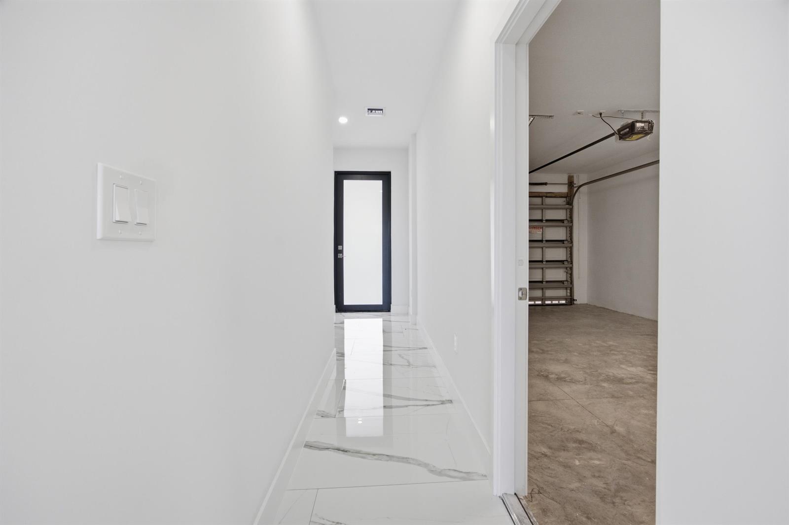 A hallway with white walls and marble-look tile flooring leads to a dark-framed glass door — 1544 NW 1st Avenue, Pompano Beach FL 33060, POMPANO BEACH, FL