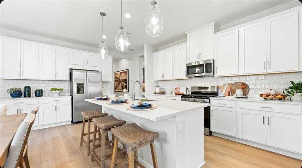 A modern kitchen features white cabinetry, a central island with bar stools, and stainless appliances — 4457 OCHOS RIOS PLACE, KISSIMMEE, FL