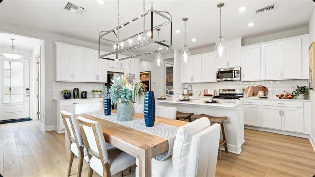 A bright kitchen and dining area feature white cabinets, light wood floors, and pendant lighting — 4457 OCHOS RIOS PLACE, KISSIMMEE, FL