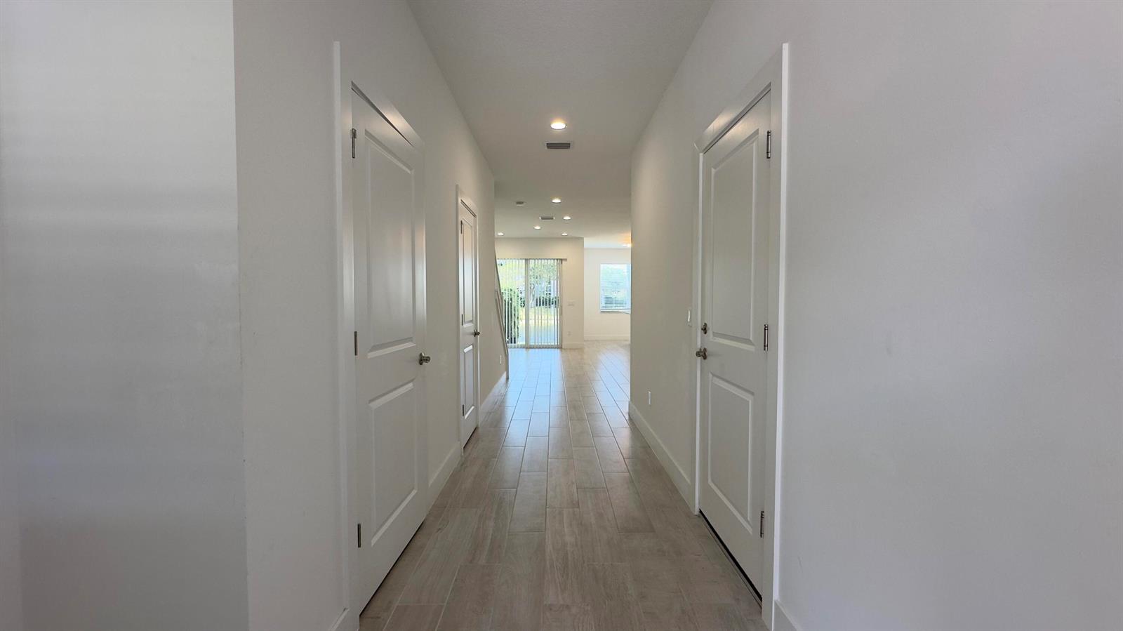A hallway with light wood-look tile flooring leads to a bright living area with sliding doors — 621 Parsons Way, Deerfield Beach FL 33442, DEERFIELD BEACH, FL