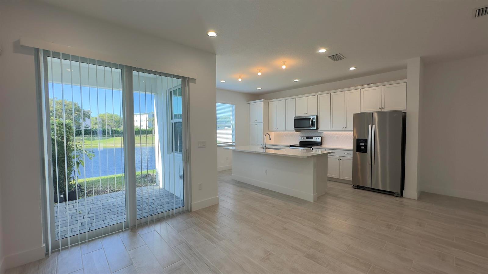 A modern kitchen features white cabinets, stainless steel appliances, and a central island overlooking a lake — 621 Parsons Way, Deerfield Beach FL 33442, DEERFIELD BEACH, FL