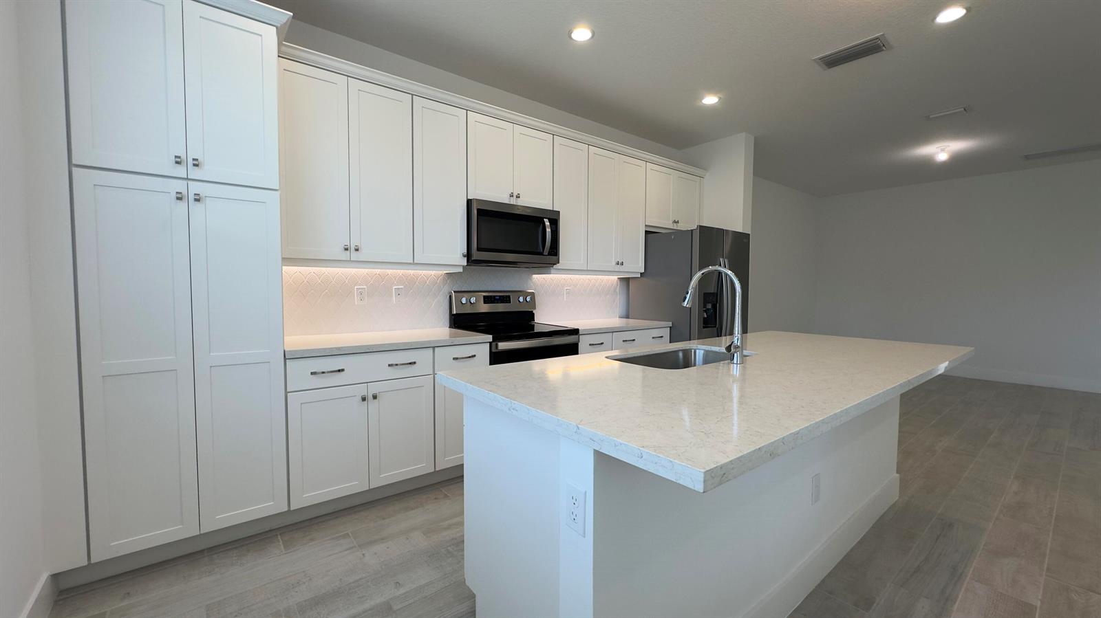 A modern kitchen features white cabinetry, quartz countertops, stainless steel appliances, and a central island — 621 Parsons Way, Deerfield Beach FL 33442, DEERFIELD BEACH, FL