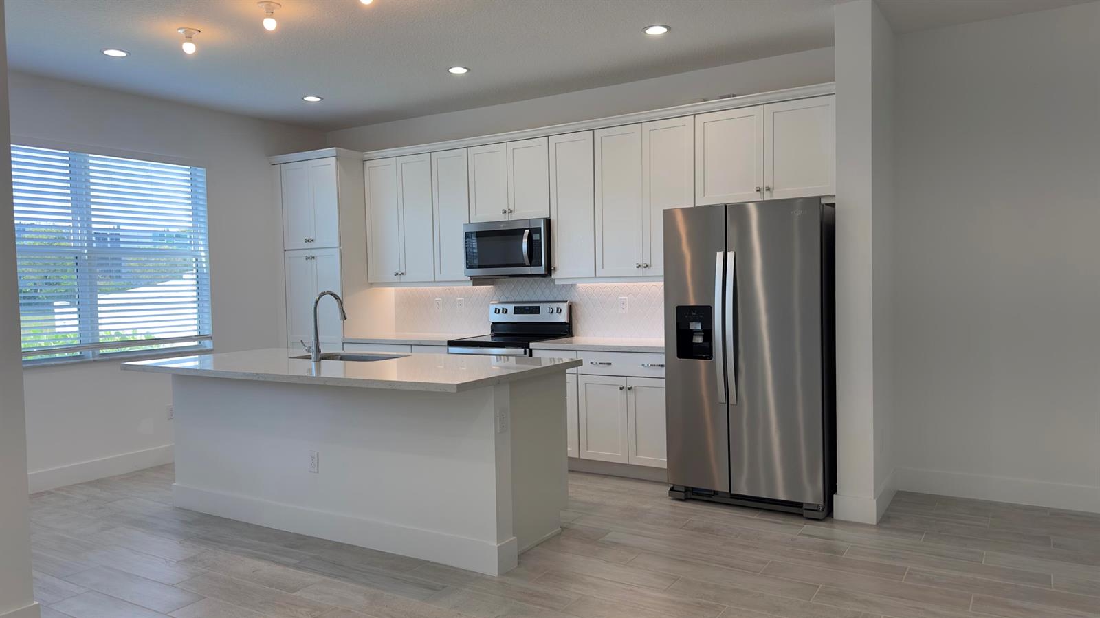 A modern kitchen features white cabinetry, stainless steel appliances, and a central island with seating — 621 Parsons Way, Deerfield Beach FL 33442, DEERFIELD BEACH, FL