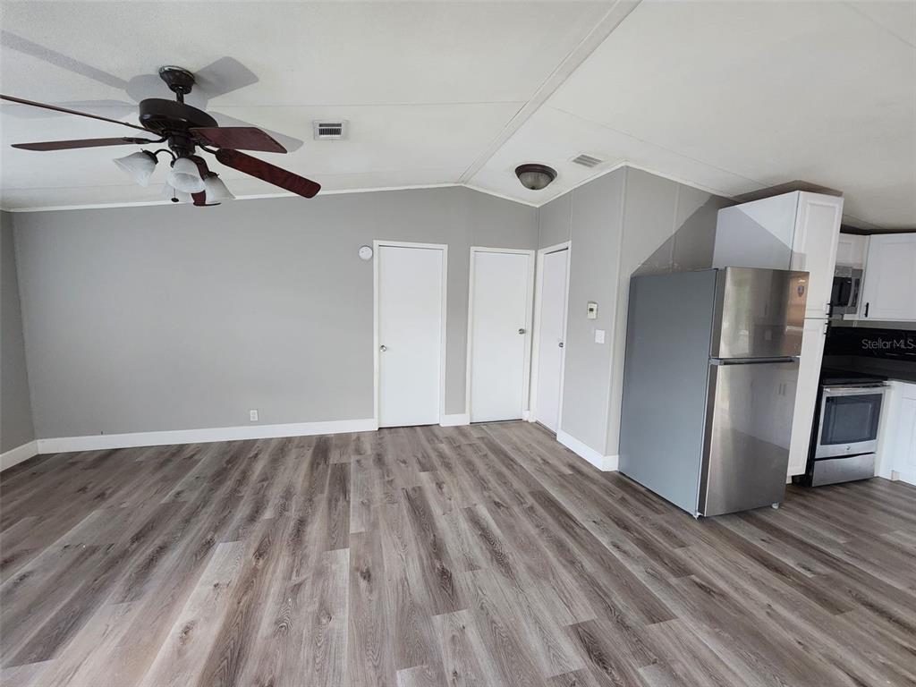 An open-concept living area features gray walls, wood-look flooring, a ceiling fan, and a kitchen — 9514 11TH AVENUE, ORLANDO, FL