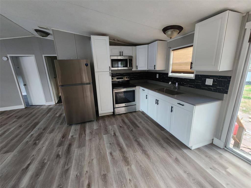 A kitchen features white cabinets, stainless steel appliances, a dark backsplash, and gray flooring — 9514 11TH AVENUE, ORLANDO, FL