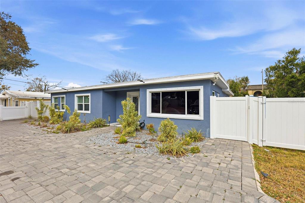 A blue single-story house features a paved driveway, a white fence, and a small garden — 2521 W CREST AVENUE, TAMPA, FL