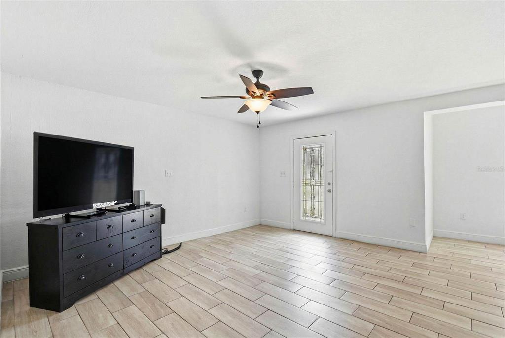 A room with light-colored tile flooring, a black dresser, a television, and a ceiling fan — 2521 W CREST AVENUE, TAMPA, FL