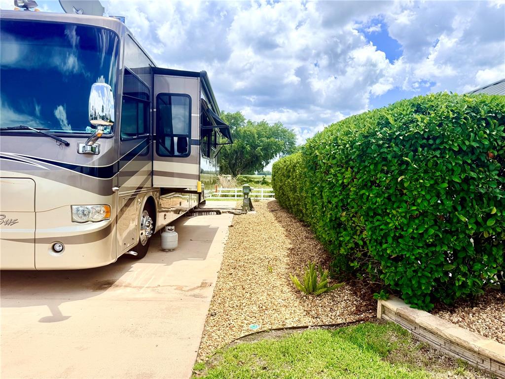 A large recreational vehicle is parked on a concrete pad next to a tall hedge — 4817 SE 94TH AVENUE, WEBSTER, FL