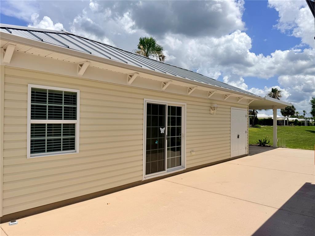The exterior of a beige house features a metal roof, sliding glass doors, and patio — 4817 SE 94TH AVENUE, WEBSTER, FL