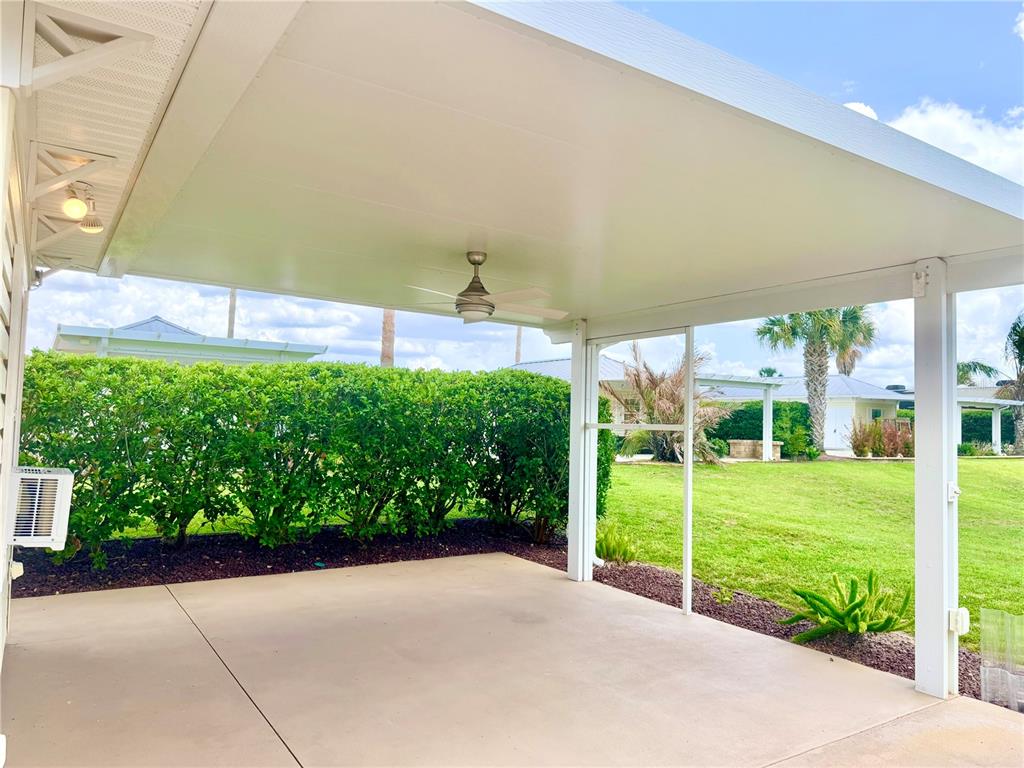 A covered concrete patio features a ceiling fan and overlooks a grassy backyard with hedges — 4817 SE 94TH AVENUE, WEBSTER, FL