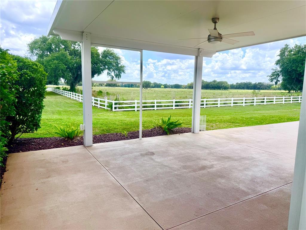 A covered concrete patio overlooks a grassy field enclosed by a white fence — 4817 SE 94TH AVENUE, WEBSTER, FL