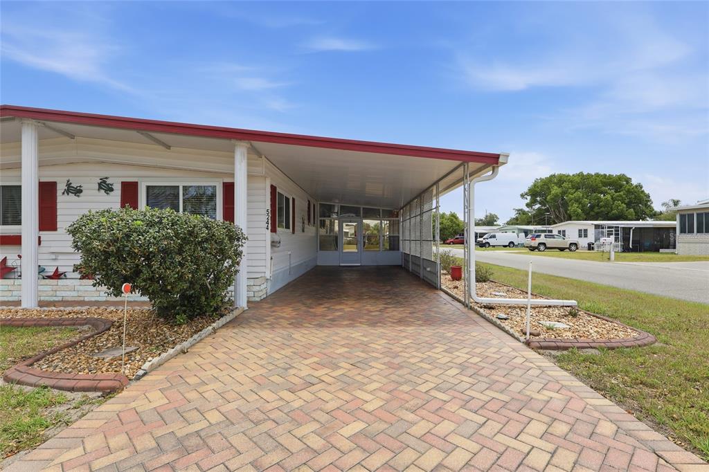 A mobile home exterior features a paved driveway, a covered carport, and a small garden — 5244 MOHAWK STREET, ZEPHYRHILLS, FL
