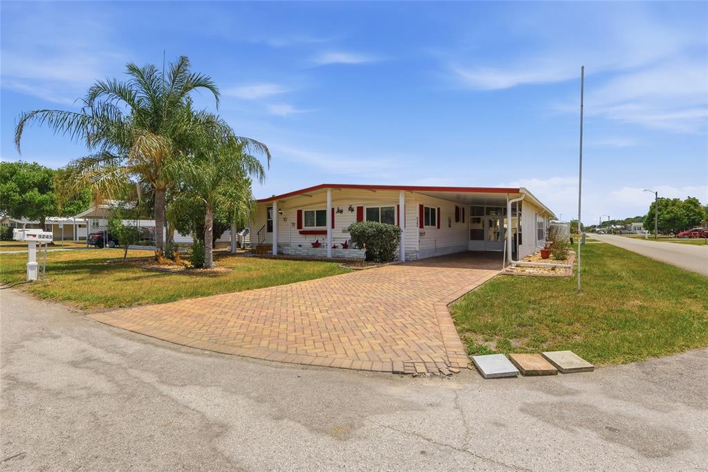 A single-story manufactured home features a brick-paver driveway, a carport, and a palm tree — 5244 MOHAWK STREET, ZEPHYRHILLS, FL