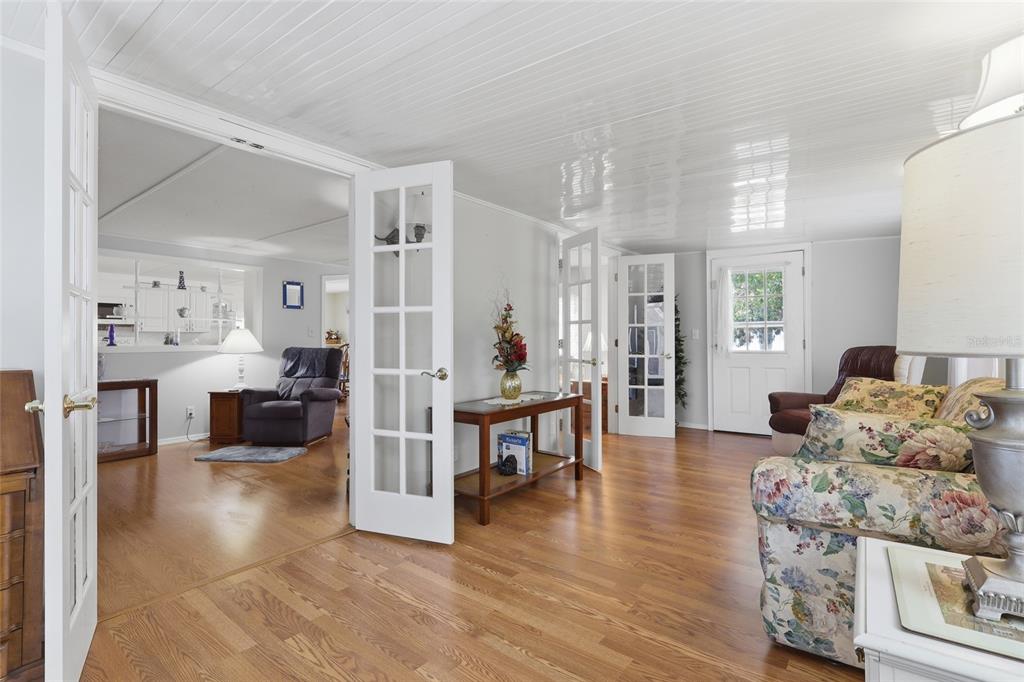 A living room with hardwood floors, white paneled ceilings, and French doors leading to another room — 5244 MOHAWK STREET, ZEPHYRHILLS, FL