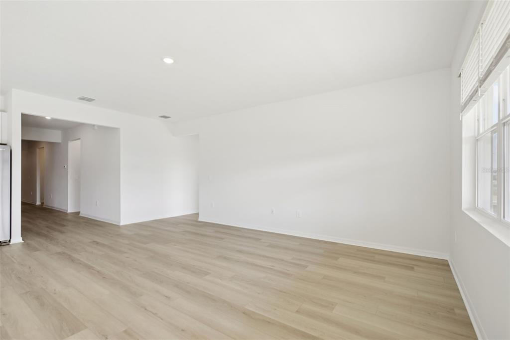 An empty living room features light wood-look flooring, white walls, and a large window — 13318 SHELLMORE AVENUE, PALMETTO, FL