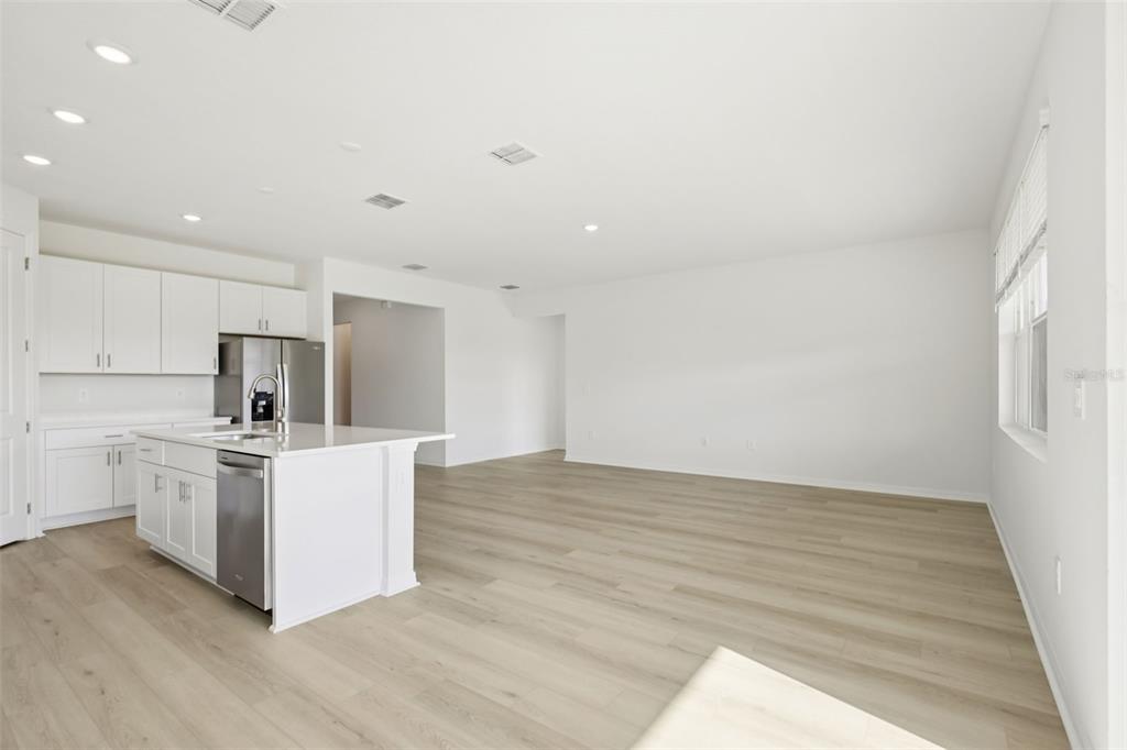 A modern kitchen with white cabinets and a center island opens into a living area — 13318 SHELLMORE AVENUE, PALMETTO, FL