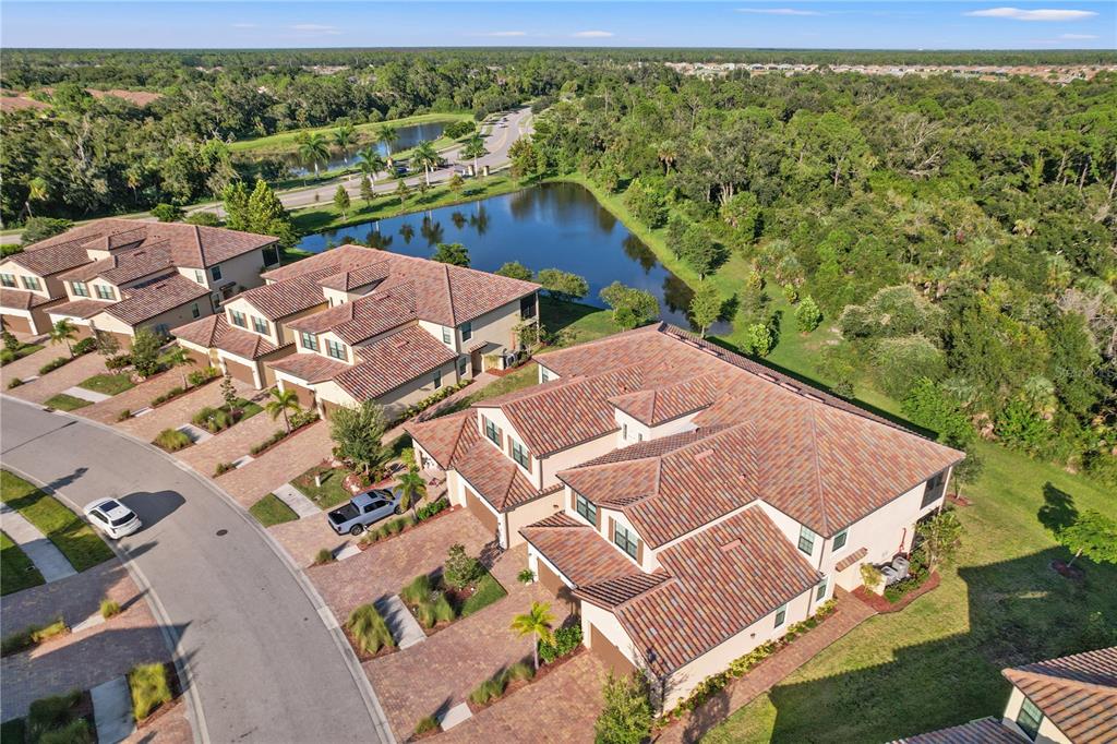 An aerial view of multi-story residential townhomes with tile roofs near a pond and woods — 12460 GHIBERTI CIRCLE UNIT 202, VENICE, FL