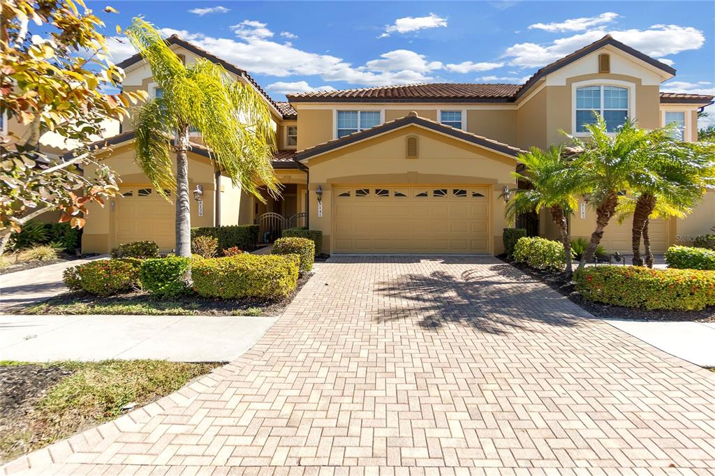 A two-story tan stucco house with a brick paver driveway and palm trees — 8141 MIRAMAR WAY UNIT 8141, LAKEWOOD RANCH, FL