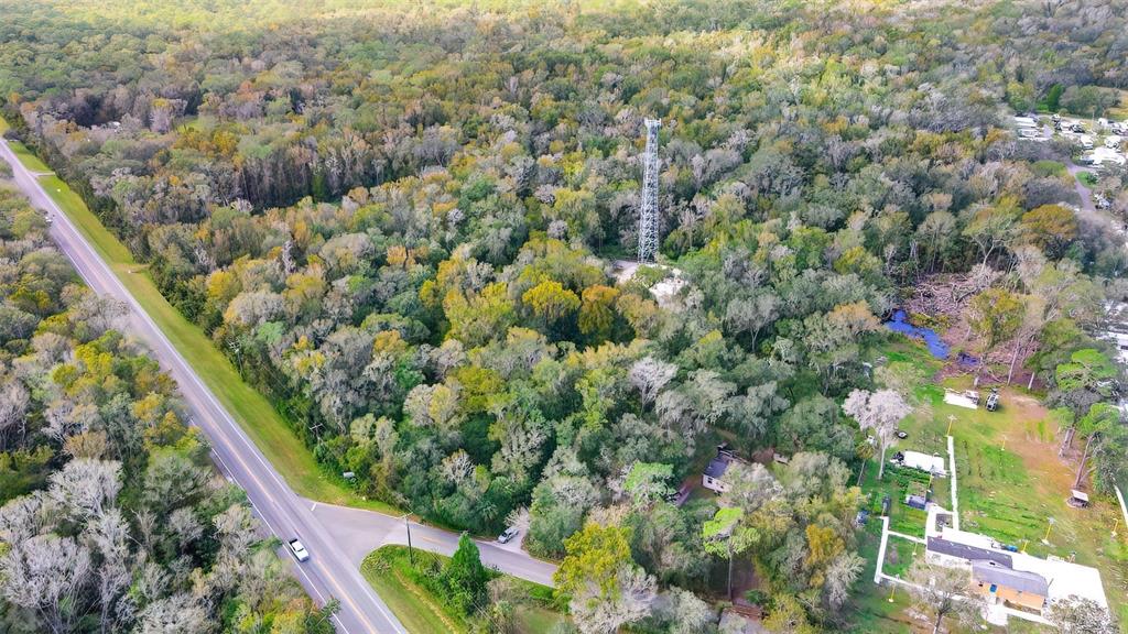 An aerial view shows a wooded lot featuring a tall communication tower and nearby houses — 14902 DEAD RIVER ROAD, THONOTOSASSA, FL