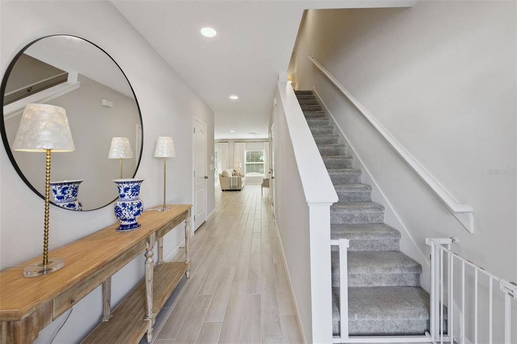 A bright hallway features light wood-look tile flooring, a wooden console table, and carpeted stairs — 3129 RIVERBOAT WAY, OVIEDO, FL