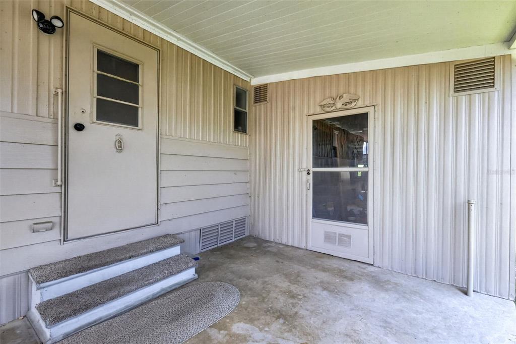 A covered concrete porch features two exterior doors, carpeted steps, and vertical siding — 488 MARINA LANE, TAVARES, FL