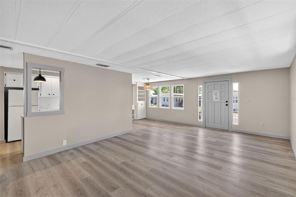 An open living area features light gray wood-look flooring, beige walls, and a pass-through window — 488 MARINA LANE, TAVARES, FL