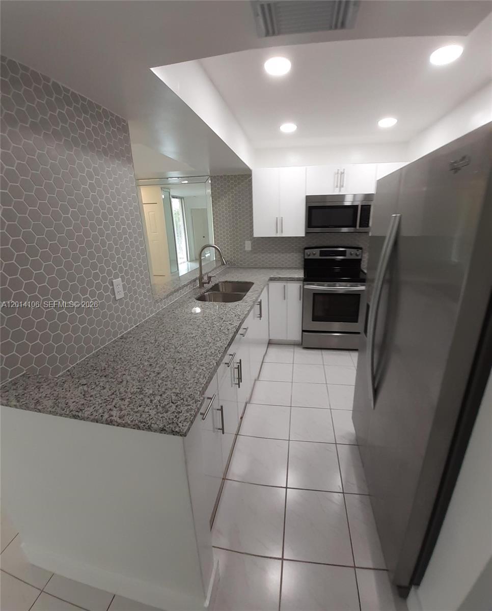 A galley kitchen features white cabinets, granite countertops, stainless steel appliances, and gray hexagonal backsplash tile — 11800 SW 18th St # 4, Miami FL 33175, MIAMI, FL