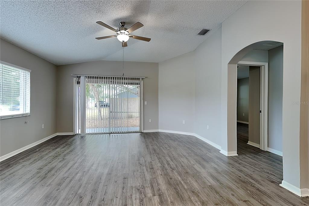 An empty living room features gray wood-look flooring, a ceiling fan, and sliding glass doors — 11759 LYNMOOR DRIVE, RIVERVIEW, FL