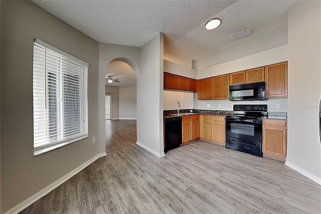 A kitchen with wood cabinets, black appliances, and granite countertops opens to a living area — 11759 LYNMOOR DRIVE, RIVERVIEW, FL