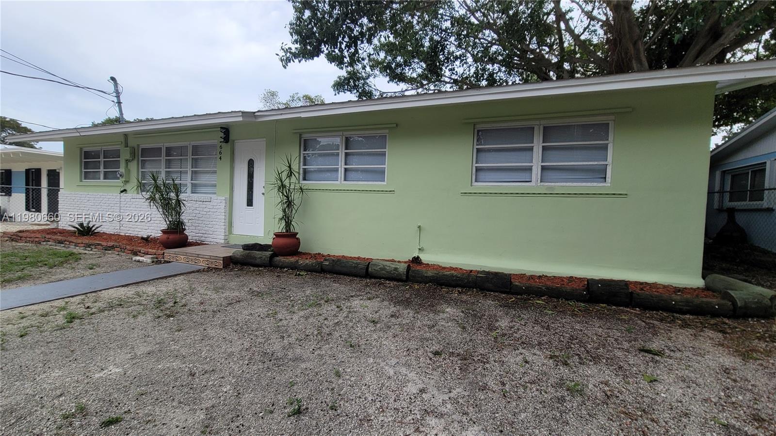 A light green single-story house features a white front door and gravel driveway — 664 Colson Dr, Key Largo FL 33037, KEY LARGO, FL