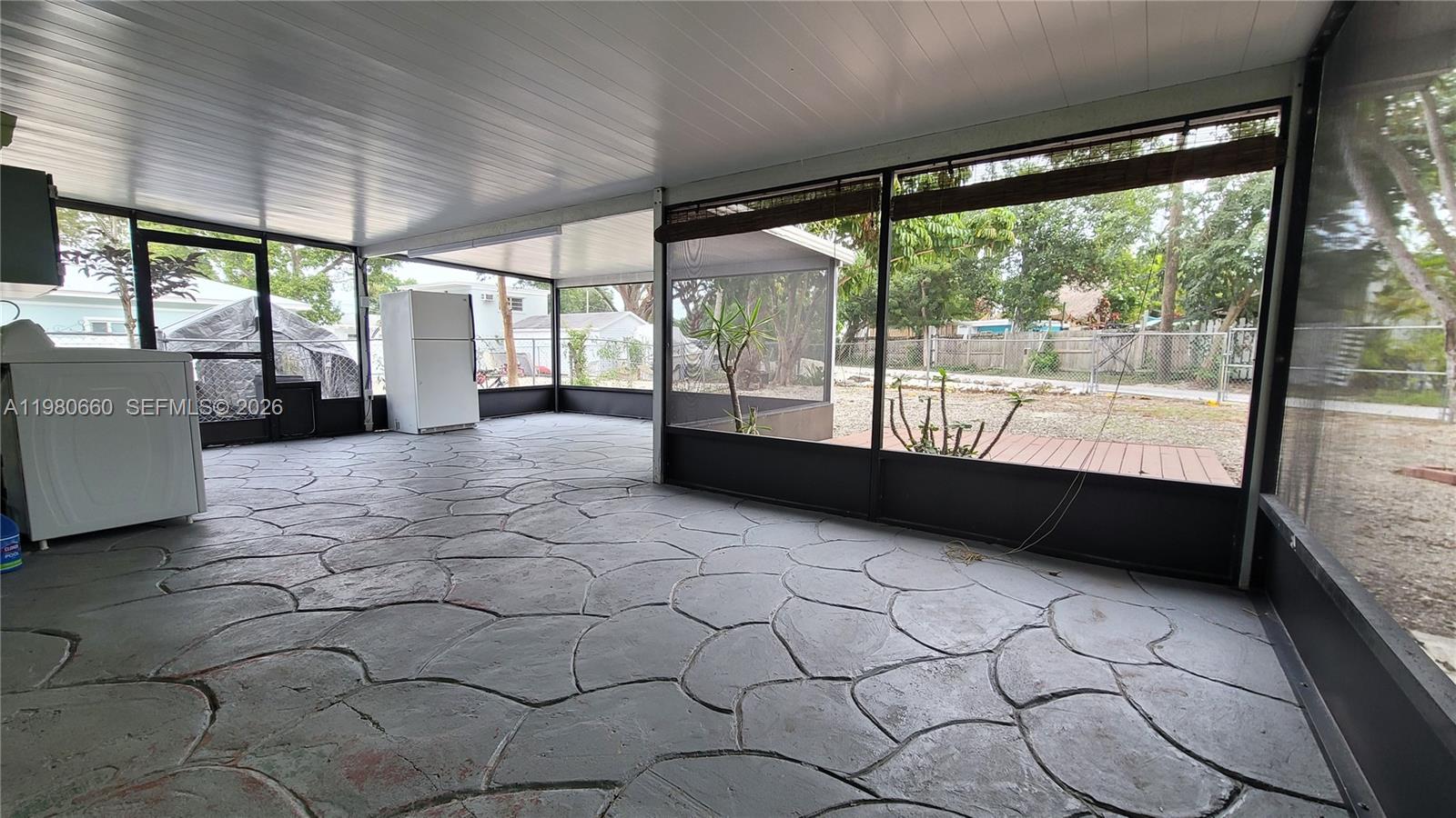A screened-in patio features a gray stone-patterned floor, a white refrigerator, and a laundry appliance — 664 Colson Dr, Key Largo FL 33037, KEY LARGO, FL