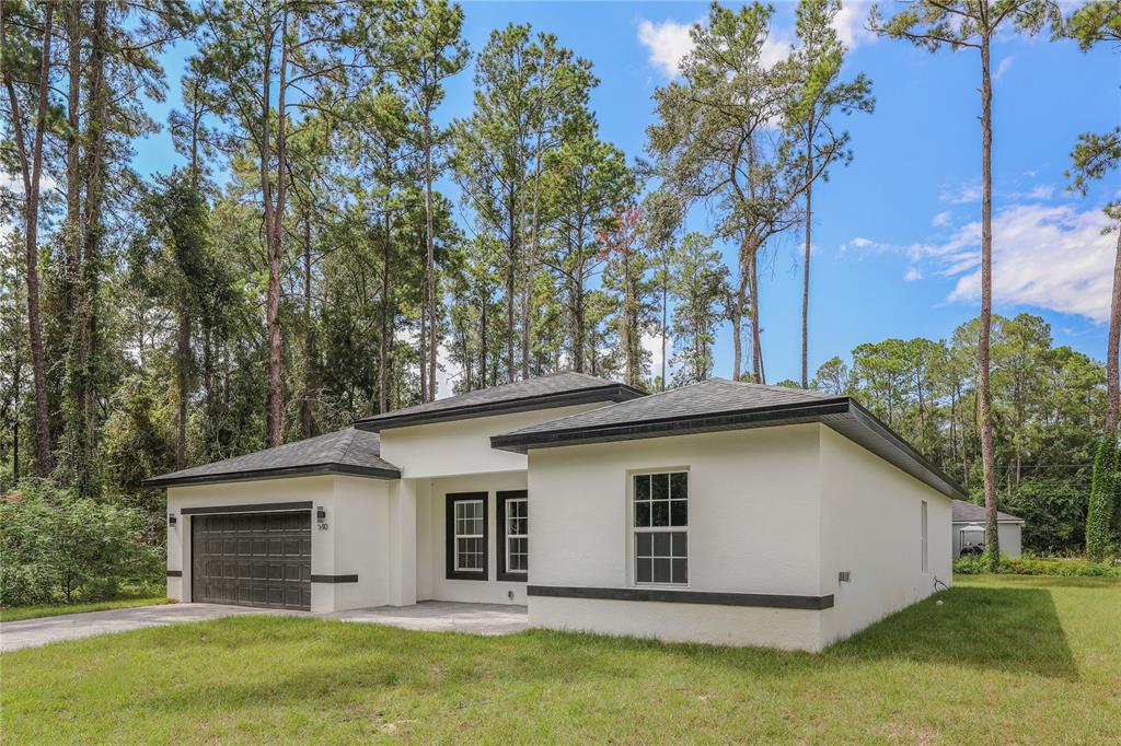 A single-story white house with a dark garage door and a flat roofline — 14519 SW 79TH AVE RD, OCALA, FL