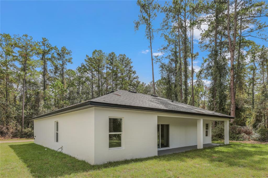 The exterior of a white, single-story house with a covered patio and surrounding trees — 14519 SW 79TH AVE RD, OCALA, FL