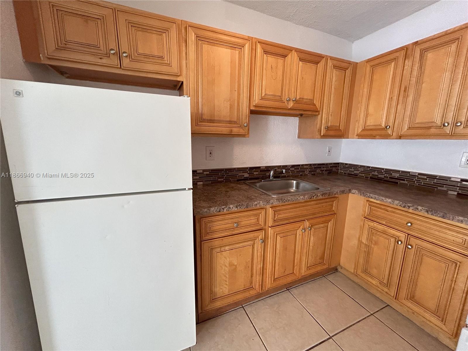 A kitchen features light wood cabinets, a white refrigerator, and a brown tiled backsplash — 8287 NE Miami Ct # 101, Miami FL 33138, MIAMI, FL