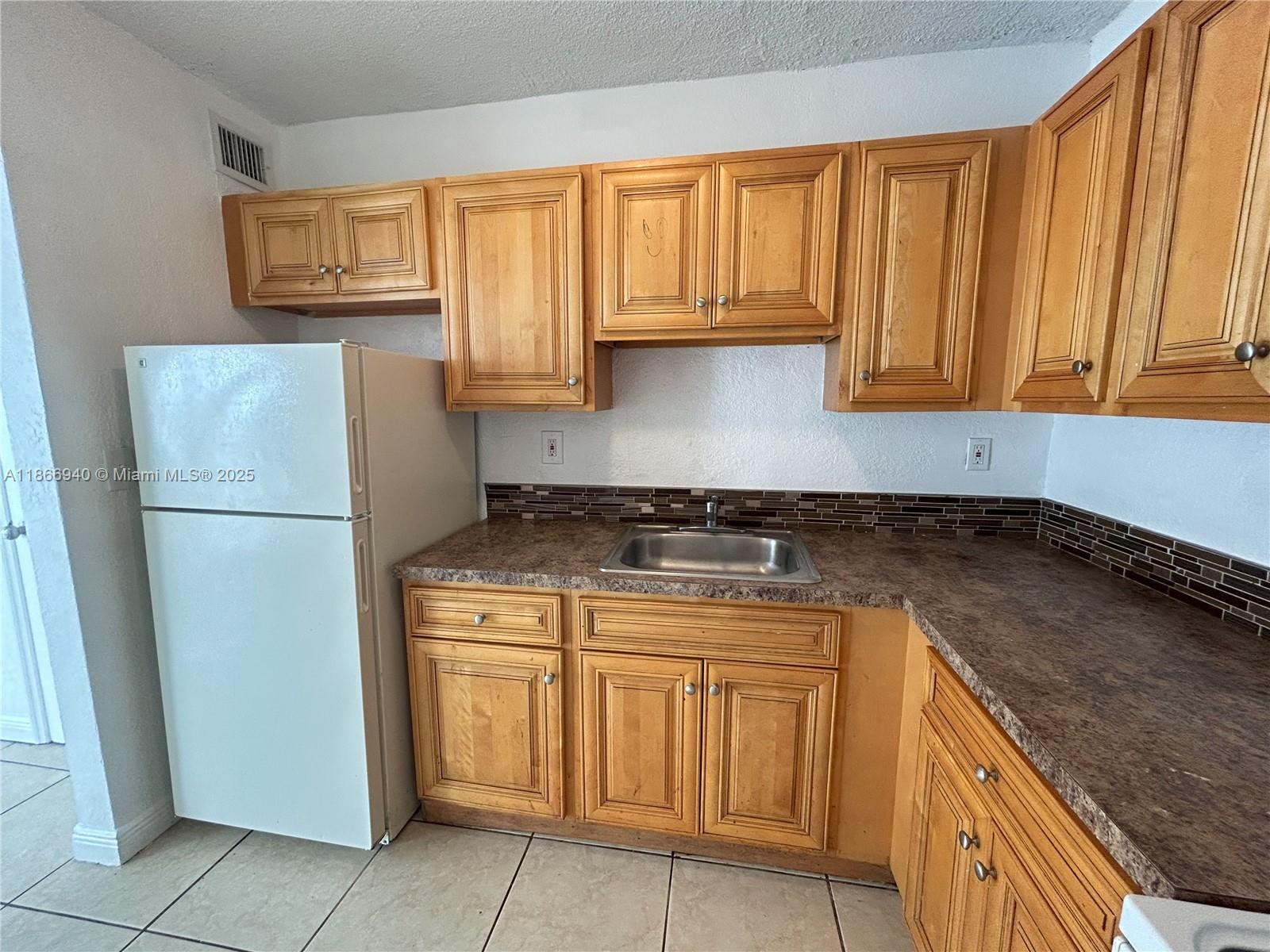 A kitchen features light wood cabinets, a white refrigerator, a stainless steel sink, and tile flooring — 8287 NE Miami Ct # 101, Miami FL 33138, MIAMI, FL