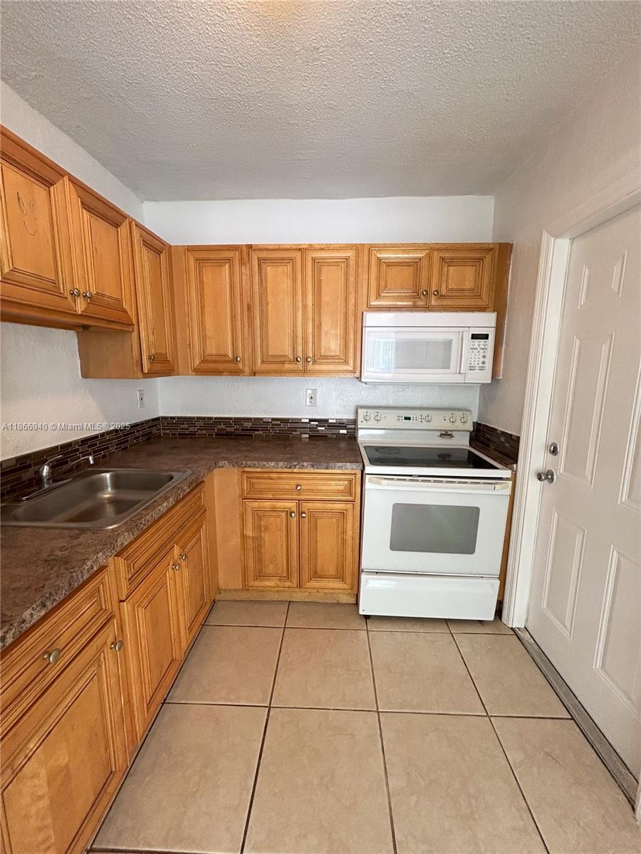 A kitchen features wood cabinets, a white stove, a microwave, and a tiled floor — 8287 NE Miami Ct # 101, Miami FL 33138, MIAMI, FL