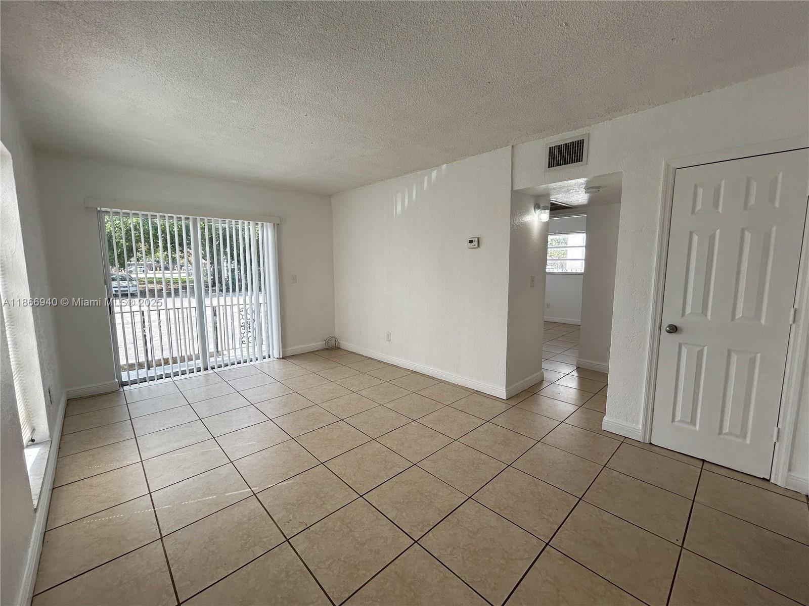 An empty room features beige tile flooring, white walls, and a sliding glass door — 8287 NE Miami Ct # 101, Miami FL 33138, MIAMI, FL