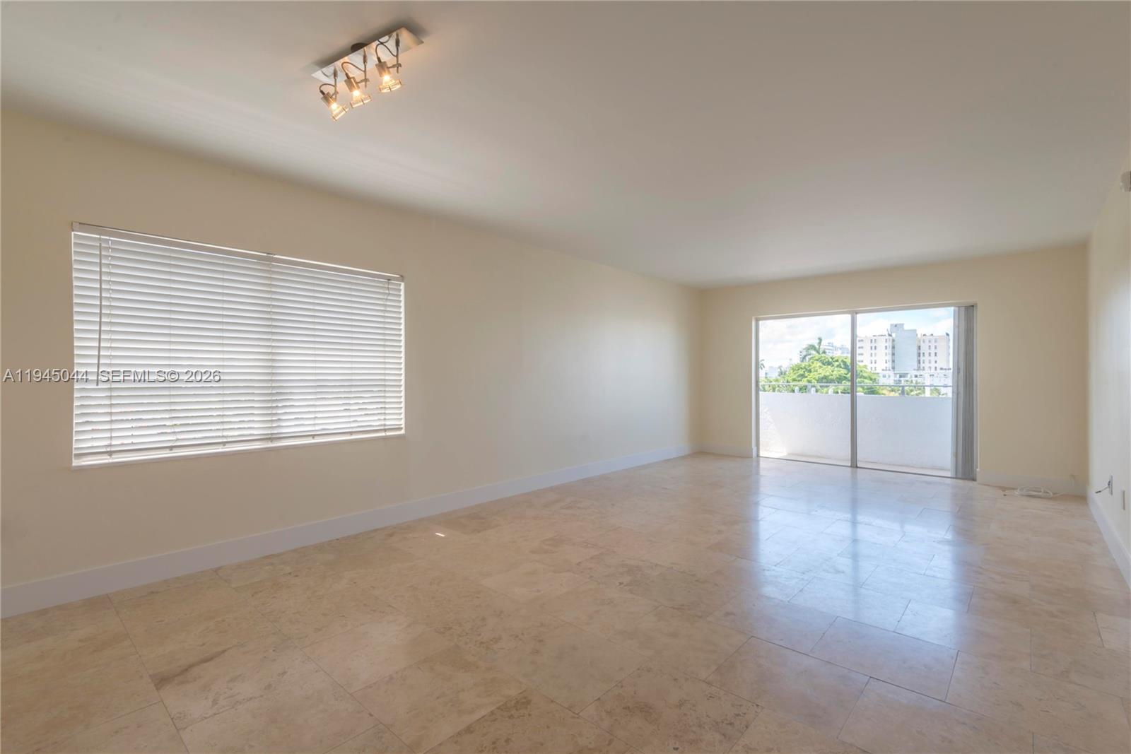 An empty room features light-colored tile flooring, a window with blinds, and a sliding glass door — 1200 14th St # 5E, Miami Beach FL 33139, MIAMI BEACH, FL