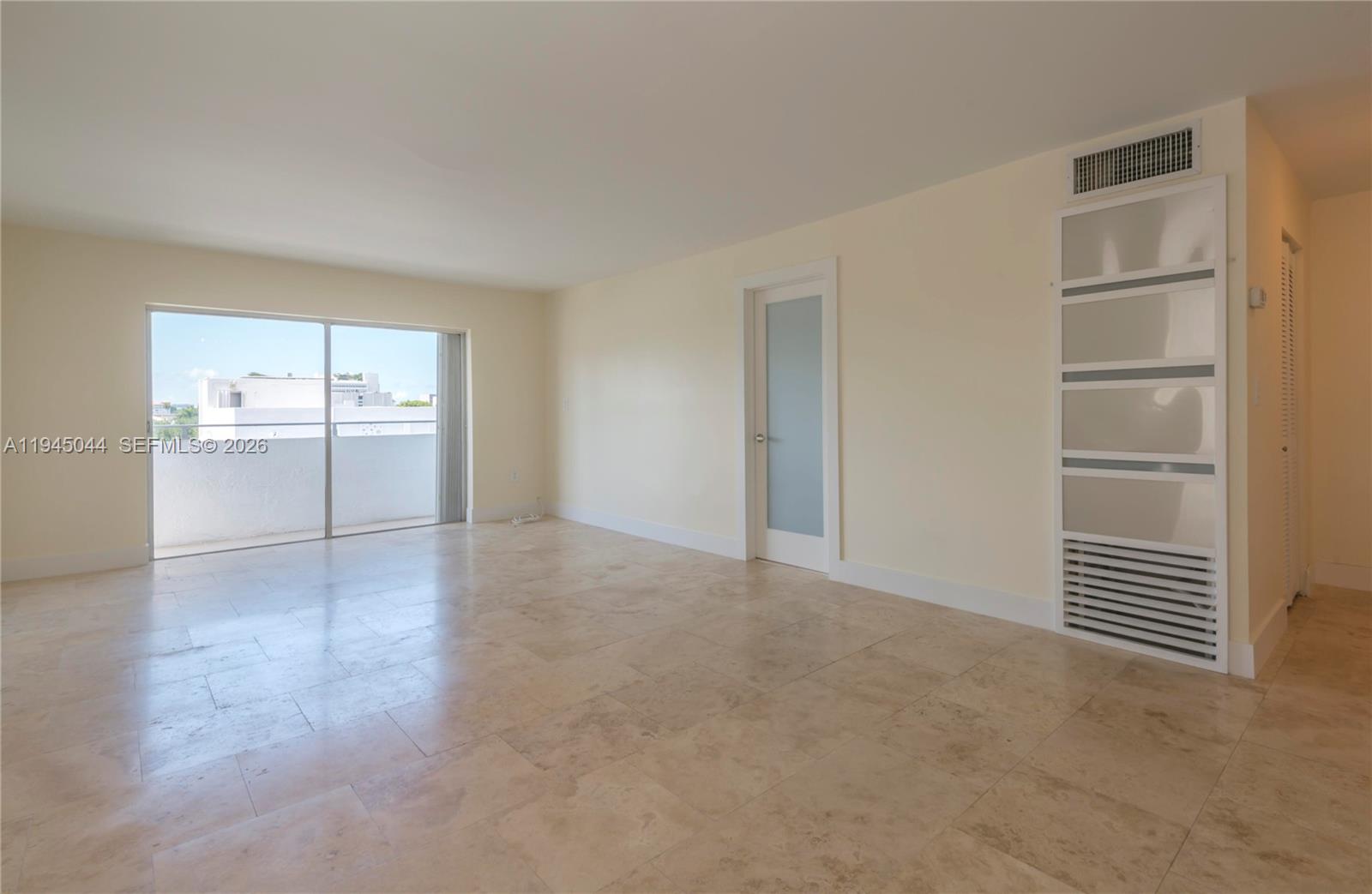 An empty living room features beige tile flooring, a glass-paneled door, and a balcony entrance — 1200 14th St # 5E, Miami Beach FL 33139, MIAMI BEACH, FL