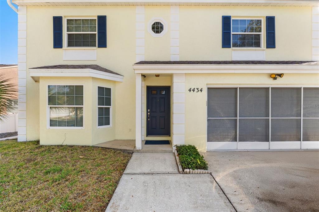 A two-story house with yellow siding, a dark front door, and a screened garage — 4434 NORTHAMPTON DRIVE, NEW PORT RICHEY, FL