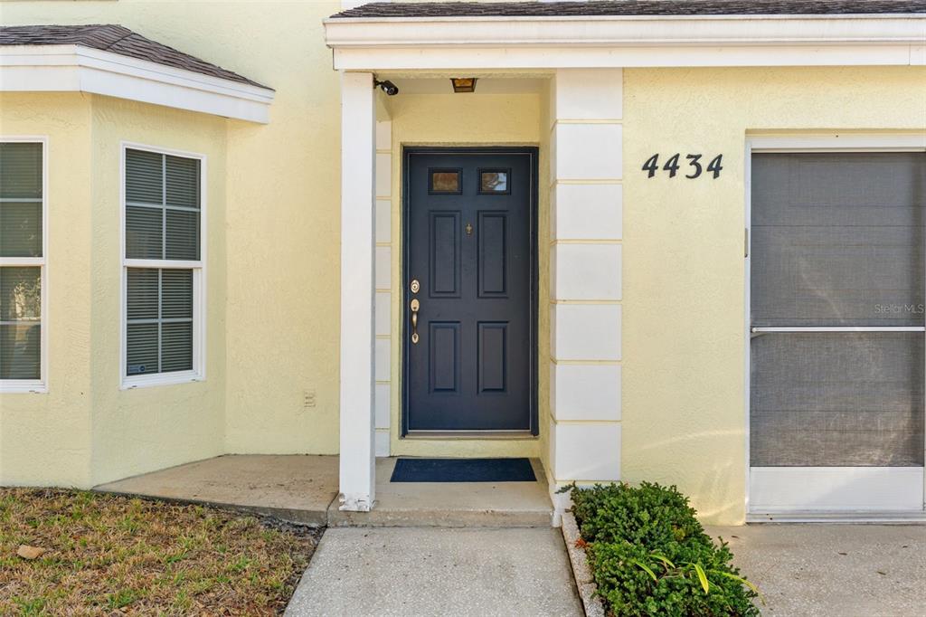 The exterior view shows a yellow house with a dark blue front door and walkway — 4434 NORTHAMPTON DRIVE, NEW PORT RICHEY, FL