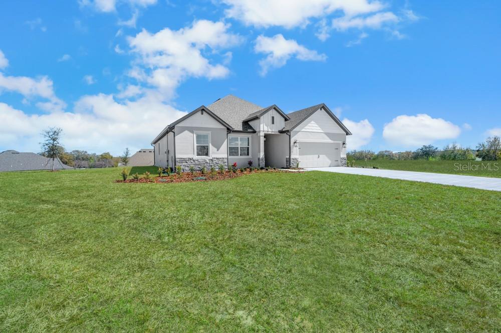 A single-story house with a white stucco facade, stone accents, and a two-car garage — 36794 SUNDOWNER TRAIL, FRUITLAND PARK, FL