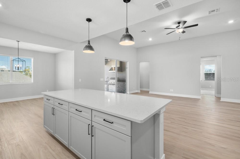A kitchen island with gray cabinets and white countertops sits in an open-concept living space — 36794 SUNDOWNER TRAIL, FRUITLAND PARK, FL