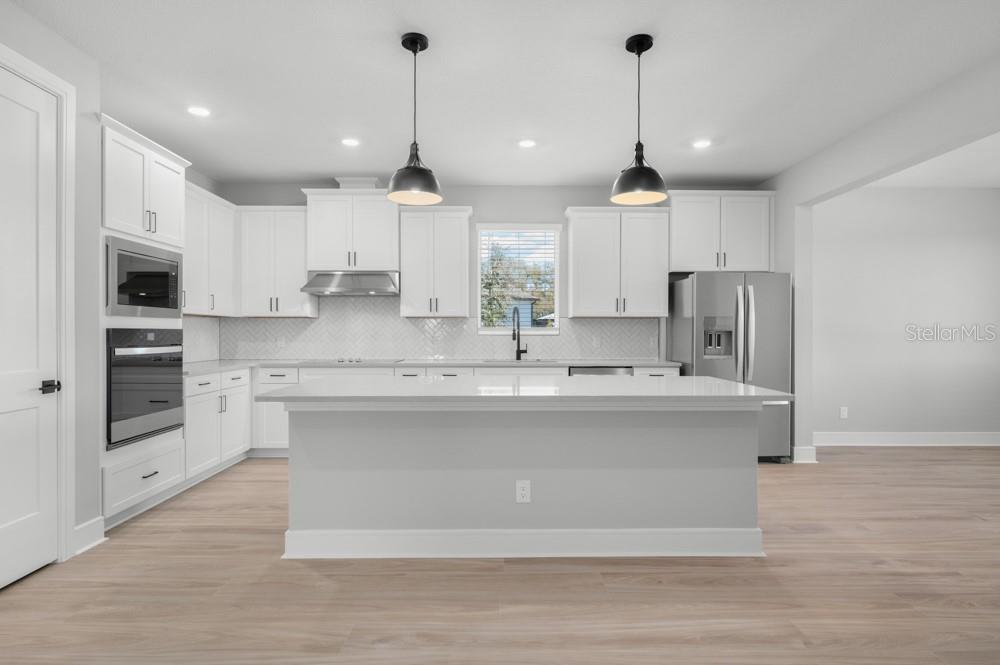A modern kitchen features white cabinetry, stainless steel appliances, a central island, and wood flooring — 36794 SUNDOWNER TRAIL, FRUITLAND PARK, FL