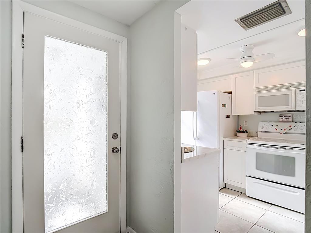 A white door with frosted glass opens into a kitchen with white cabinets and appliances — 4227 TOUCHTON PLACE UNIT 4227, NEW PORT RICHEY, FL