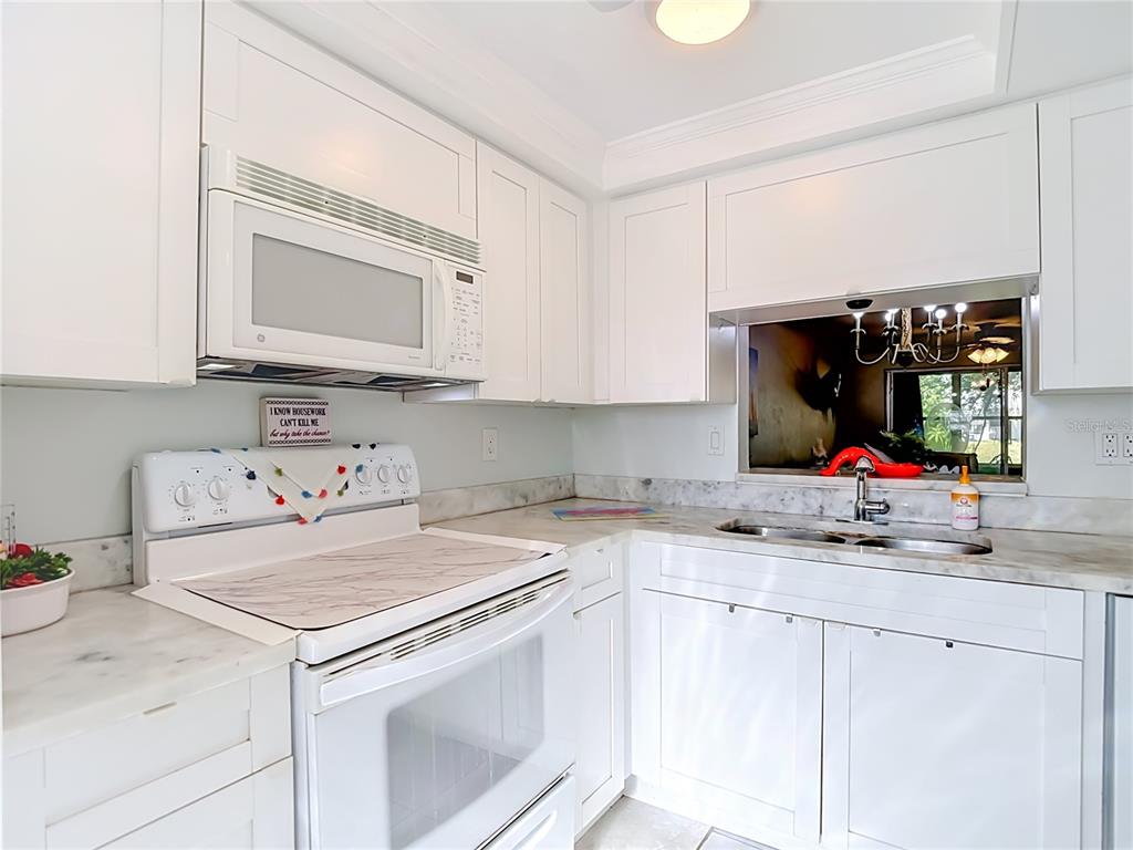 A white kitchen features marble-look countertops, white cabinetry, a microwave, and a pass-through window — 4227 TOUCHTON PLACE UNIT 4227, NEW PORT RICHEY, FL