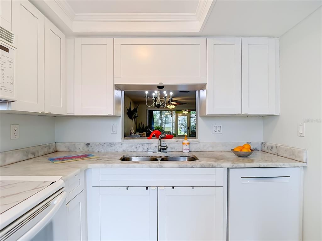A white kitchen features marble countertops, a double sink, and a pass-through window — 4227 TOUCHTON PLACE UNIT 4227, NEW PORT RICHEY, FL
