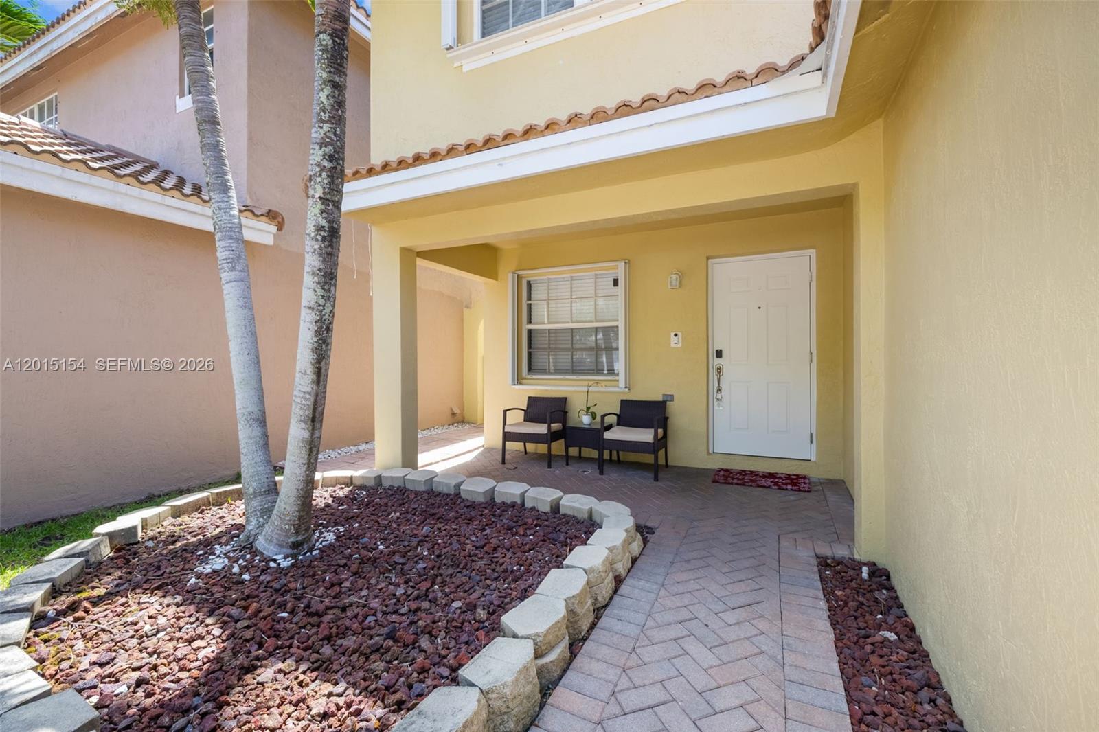 A yellow house exterior features a covered entryway with a brick walkway and two chairs — 9288 NW 55th St, Sunrise FL 33351, SUNRISE, FL